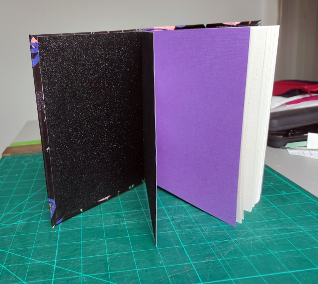 The books standing upright, opened in a way to show the glittery-black endpapers and the two following purple pages. The books standing upright, opened in a way to show the glittery-black endpapers and the two following purple pages.