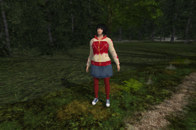 Me in a red and cream hoodie, a blue denim miniskirt, striped red knit tights and blue and grey sneakers, standing by the side of a path in front of a forest