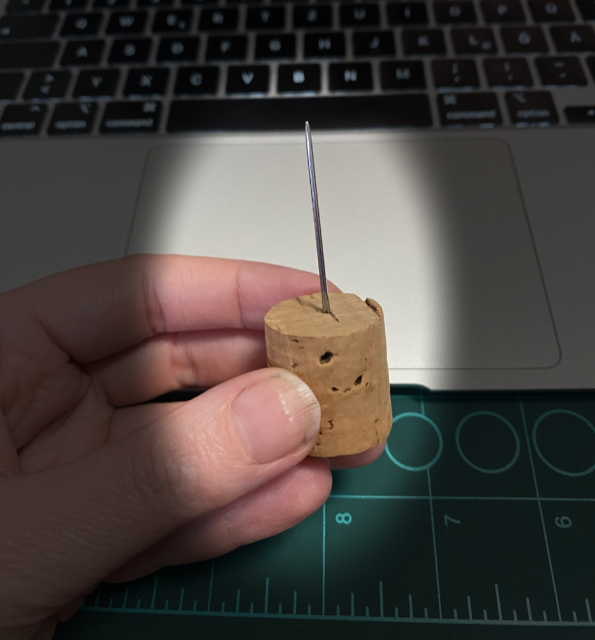 I’m holding a needle that’s stuck in a cork. I’m holding a needle that’s stuck in a cork.