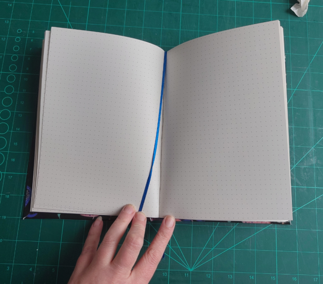 The opened book. Light gray pages with a light gray dot grid. In the middle a blue ribbon lies. The opened book. Light gray pages with a light gray dot grid. In the middle a blue ribbon lies.