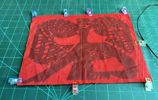 Red cloth with a worn out logo that looks like some woodcarved monster is clipped to black material. Red cloth with a worn out logo that looks like some woodcarved monster is clipped to black material.