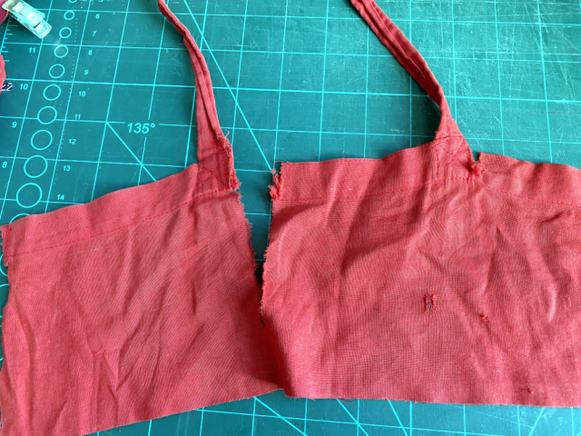 The top part of a red tote bag has been cut off. It shows a big tear in the middle of the straps and a smaller tear next to the right strap. Little holes are scattered over the cloth. The top part of a red tote bag has been cut off. It shows a big tear in the middle of the straps and a smaller tear next to the right strap. Little holes are scattered over the cloth.