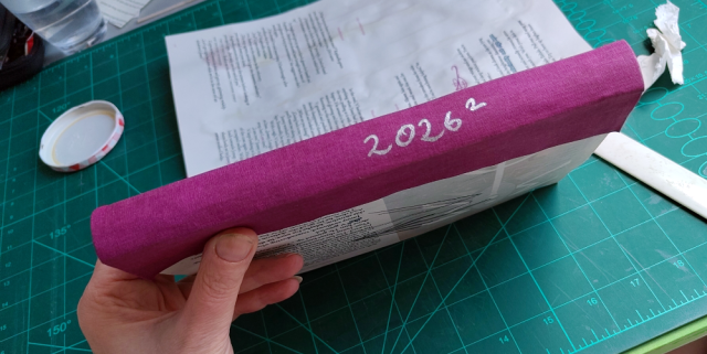 A textblock that a berry-coloured cloth has been glued on as the spine. It says '2026/2' in silver numbers. A textblock that a berry-coloured cloth has been glued on as the spine. It says '2026/2' in silver numbers.
