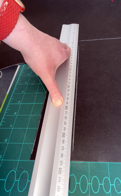 An aluminium ruler being held down on black material with white chalk lines. An aluminium ruler being held down on black material with white chalk lines.