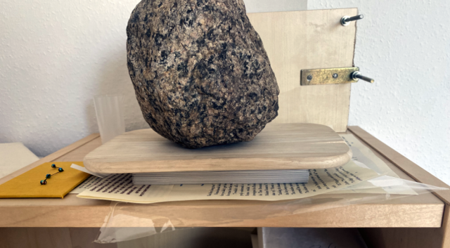 The folded signatures are stack on top each other beneath a wooden plate beneath a rock. The folded signatures are stack on top each other beneath a wooden plate beneath a rock.